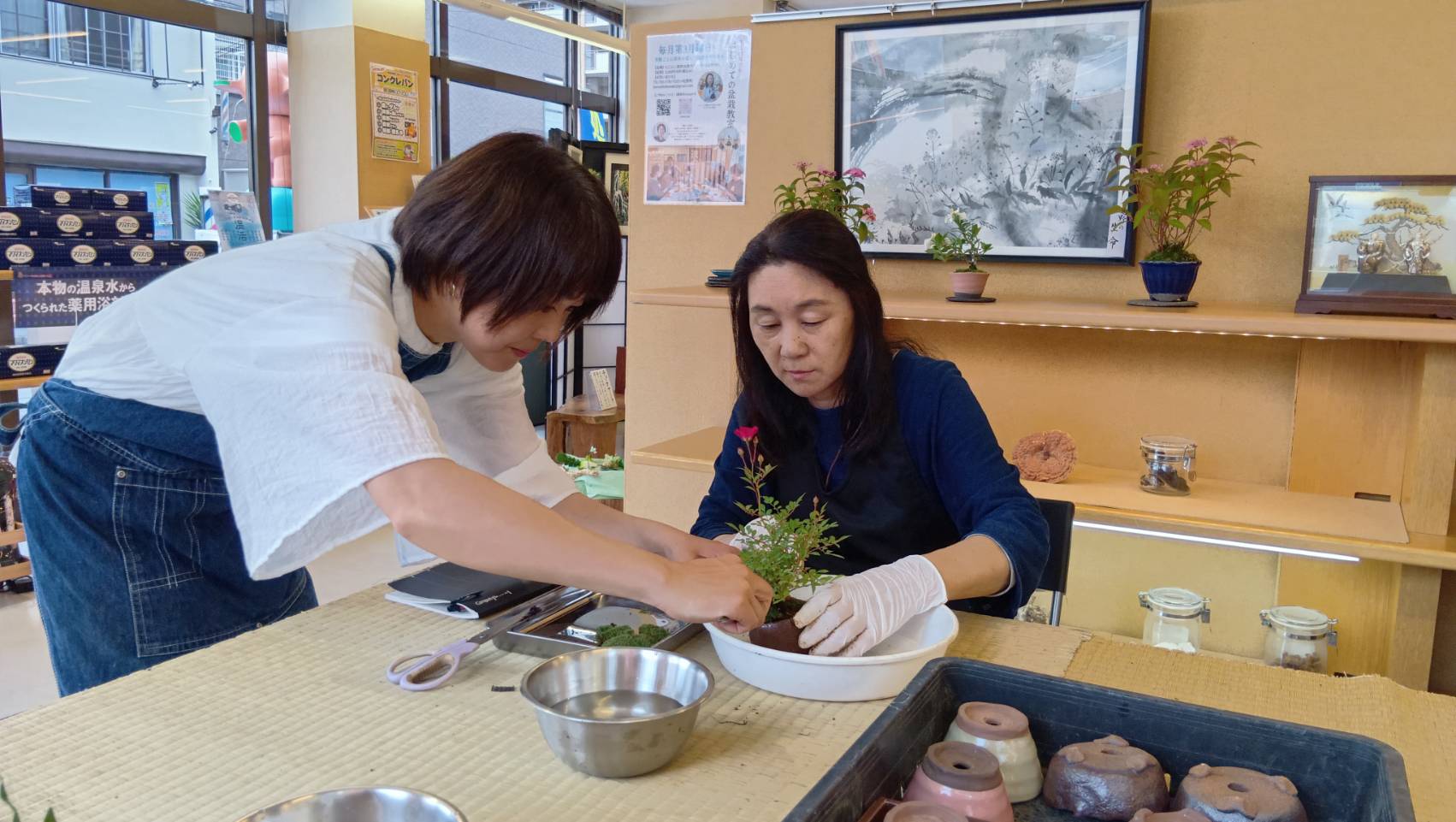 にこにこ薬局の盆栽教室で講師が参加者に手を添えて指導する様子